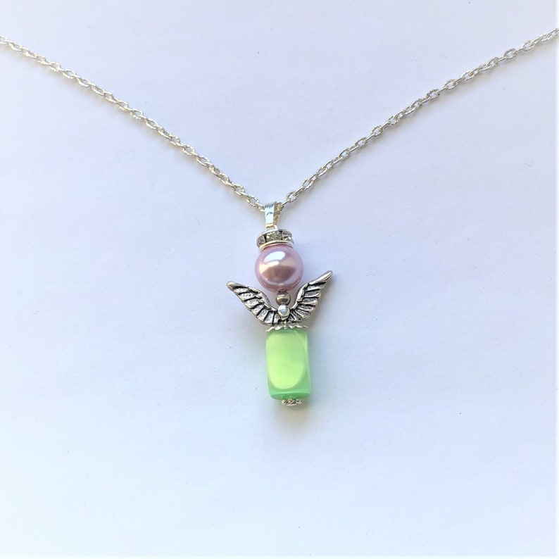 May include: A silver chain necklace with a green glass bead and a silver angel charm with a pink pearl on top.