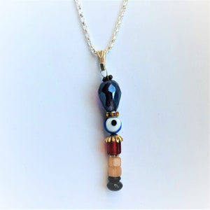 May include: A silver chain necklace with a pendant featuring a dark blue faceted bead, a blue and white evil eye bead, a red bead, a light brown bead, and a black bead.