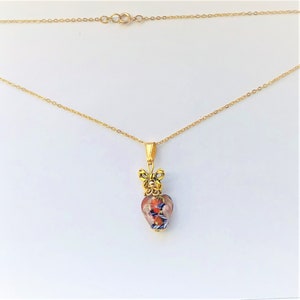 May include: A gold chain necklace with a heart-shaped pendant. The pendant is made of glass with a multi-colored pattern and a gold bow at the top.