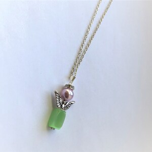 May include: A silver chain necklace with a green stone pendant and a pink pearl. The pendant features a silver angel wing design.