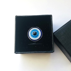 May include: A blue evil eye charm with white and silver glitter in a black velvet box.