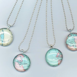 May include: Four silver necklaces with round glass pendants featuring vintage maps of different locations. The maps are printed in shades of blue, green, and pink.