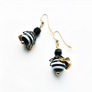 May include: A pair of gold dangle earrings with black and white striped glass beads and gold accents. The beads are shaped like a bee.
