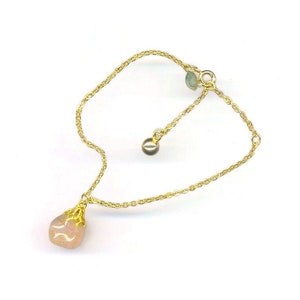 Puede incluir: Un delicado brazalete de cadena dorada con un colgante de piedra rosa. El colgante est&aacute; engastado en un dise&ntilde;o de filigrana dorada. El brazalete tiene una longitud ajustable.