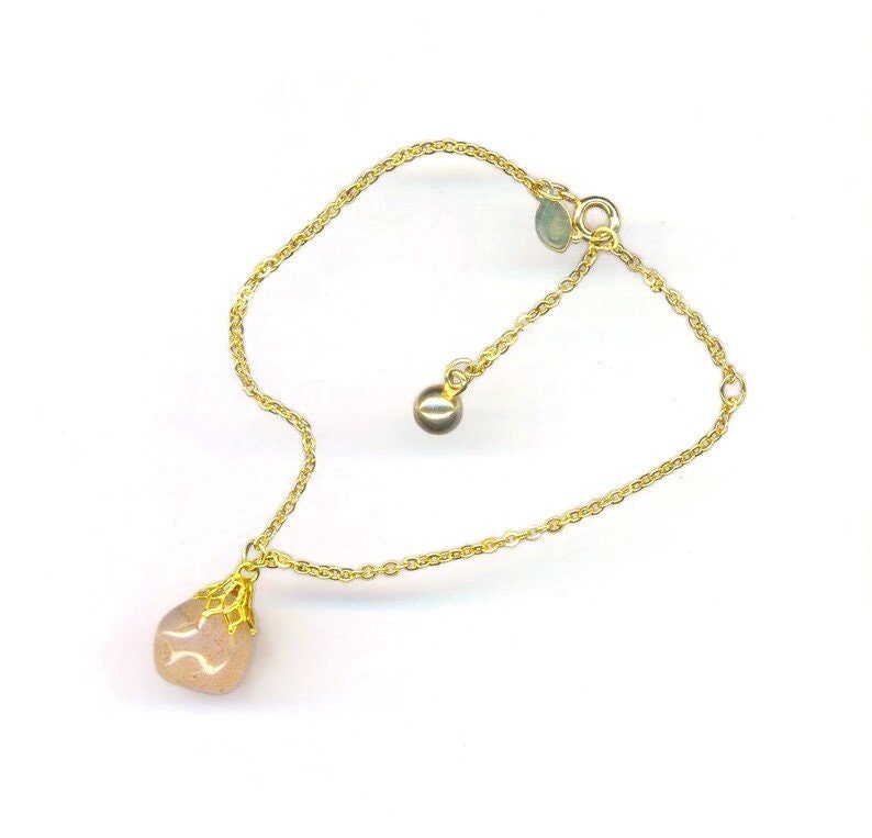 Puede incluir: Un delicado brazalete de cadena dorada con un colgante de piedra rosa. El colgante est&aacute; engastado en un dise&ntilde;o de filigrana dorada. El brazalete tiene una longitud ajustable.