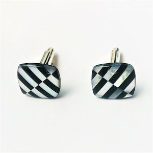 May include: A pair of black and white checkered cufflinks with a silver backing.