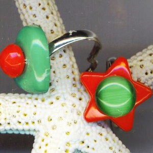 May include: Two green and red star-shaped rings with a white background. The rings are made of plastic and have a shiny finish.