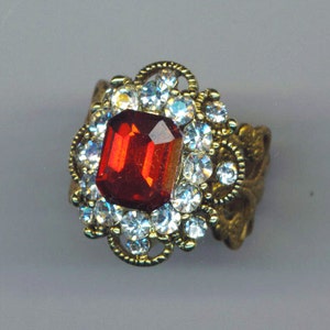 Peut inclure: Une bague en or avec une pierre précieuse rouge entourée de strass transparents.
