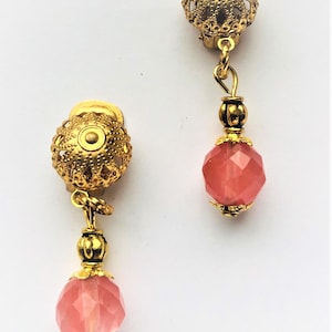 May include: A pair of gold tone clip-on earrings with a pink faceted glass bead dangling from each. The earrings have a filigree design.