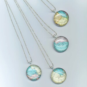May include: Four silver necklaces with round glass pendants featuring vintage maps of different locations. The maps are printed in shades of blue, green, yellow, and pink.