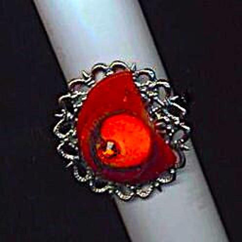 Puede incluir: Un anillo de plata con una piedra preciosa roja y naranja engastada en un dise&ntilde;o de filigrana.