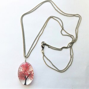 May include: A silver chain necklace with a pendant featuring a red tree encased in clear resin.