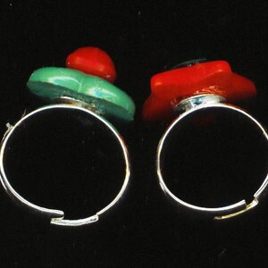 May include: Two silver rings with red and green glass stones. The rings are simple and elegant.