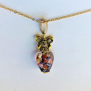 May include: A gold chain necklace with a heart-shaped pendant. The pendant is made of clear glass with colorful flecks and a gold bow at the top.