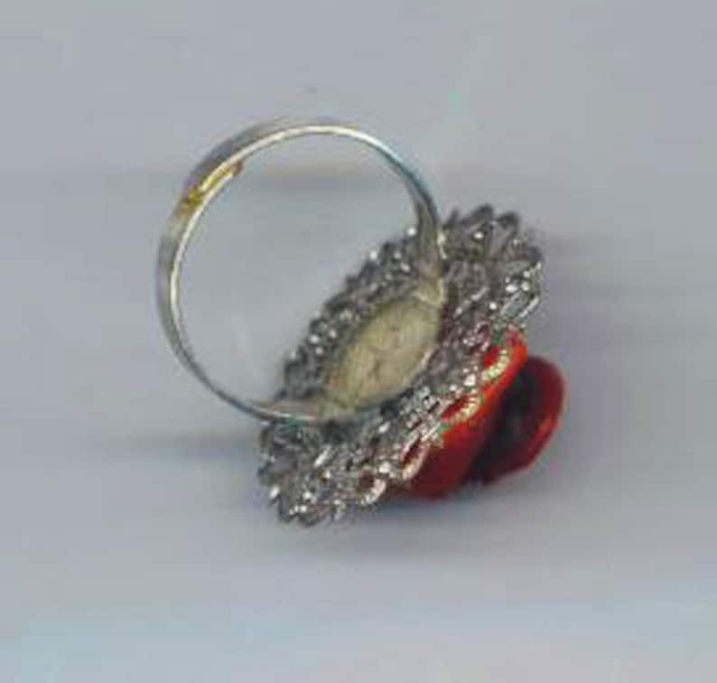 Puede incluir: Un anillo de cabuj&oacute;n rojo con un engaste de filigrana plateada. El anillo est&aacute; sobre un fondo blanco.