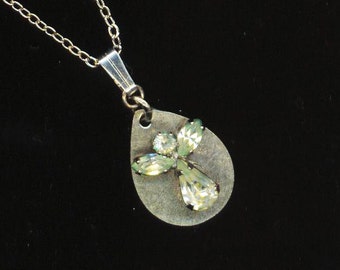 May include: A silver necklace with a teardrop-shaped pendant featuring a silver angel with clear and green rhinestones.