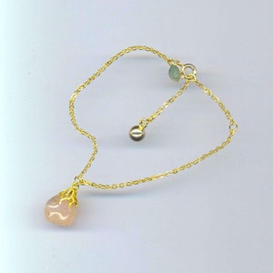 Puede incluir: Un brazalete de cadena dorada con un colgante de piedra rosa y un peque&ntilde;o acento de piedra verde. El brazalete tiene una longitud ajustable.