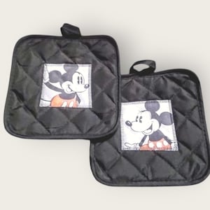 May include: Two black quilted pot holders with a Mickey Mouse graphic. Each square pot holder has a diamond pattern and a small loop for hanging. The Mickey Mouse graphic is in the center of each pot holder.