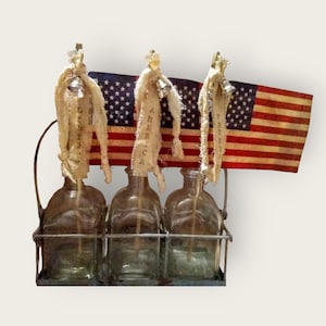 May include: Three clear glass bottles with a wire rack, each bottle has a small American flag and a fabric ribbon with the words "Liberty", "America", and "United" written on them.