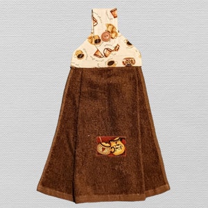 May include: Brown kitchen towel with a coffee cup design on the top and a brown and white coffee pot design on the bottom.