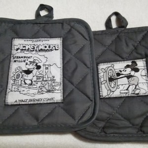 May include: A pair of gray quilted oven mitts with Mickey Mouse designs. One mitt features Mickey Mouse driving a steamboat with the text "Mickey Mouse Steamboat Willie" and "A Walt Disney Comic". The other mitt features Mickey Mouse steering a ship's wheel.