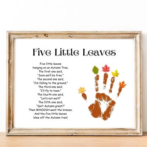May include: Framed artwork featuring a handprint with colorful leaf cutouts. The text reads "Five Little Leaves" and includes a poem about autumn. The frame is a light brown color, and the background is white.