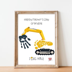 Peut inclure: Impression encadrée avec un bras de pelle jaune, une empreinte de main bleue et une empreinte de pied jaune. Le texte dit "Happy Father's Day Grandpa!" et "I DIG YOU!" avec un cœur et un nom. Le cadre est de couleur marron clair.