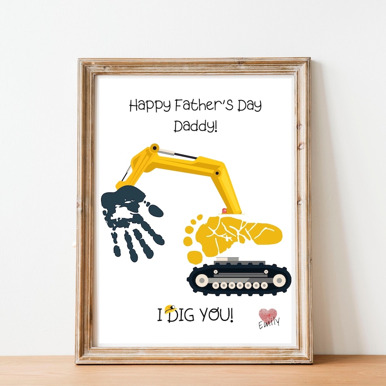 May include: Framed print with a Father's Day theme. The artwork features a yellow excavator arm, a handprint, and a footprint, with the text "Happy Father's Day Daddy!" and "I dig you!" in black. A heart and the name "Emily" are also included.