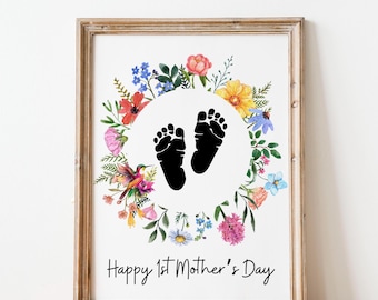 May include: A white card with a floral wreath surrounding a circle with two black baby footprints. The text "Happy 1st Mother's Day" is printed below the wreath.
