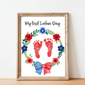 Könnte beinhalten: Gerahmter Druck mit dem Text "My First Labor Day". Der Druck zeigt rote Fußabdrücke, einen Blumenkranz mit roten und blauen Blumen und eine rot-weiß-blaue Schleife. Der Rahmen ist hellbraun.