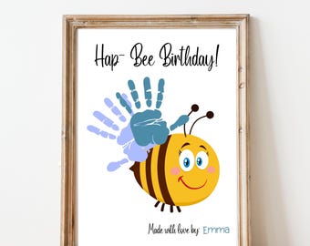 Può includere: Stampa incorniciata con un'ape dei cartoni animati gialla e marrone con un volto sorridente e un'ala a forma di impronta. Il testo recita "Hap-Bee Birthday!" e "Made with love by: Emma".