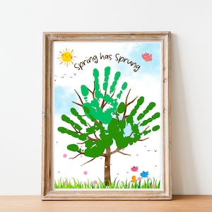 Puede incluir: Una obra de arte enmarcada con un árbol hecho de huellas de manos verdes, con el texto "Spring has Sprung". La obra incluye un sol amarillo, pájaros y hierba con flores. El marco es de color marrón claro.
