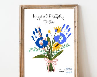 May include: A framed print with a bouquet of flowers made from handprints in blue and yellow, tied with a pink ribbon. The text "Happiest Birthday to You" is at the top. The print is signed "Max & Judith".