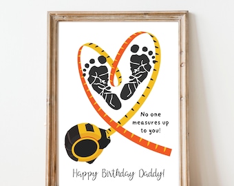 Può includere: Stampa incorniciata con un cuore formato da un metro a nastro giallo e arancione, che racchiude due impronte di piedini di bambino neri. Il testo recita "Nessuno ti misura!" e "Buon compleanno papà!"