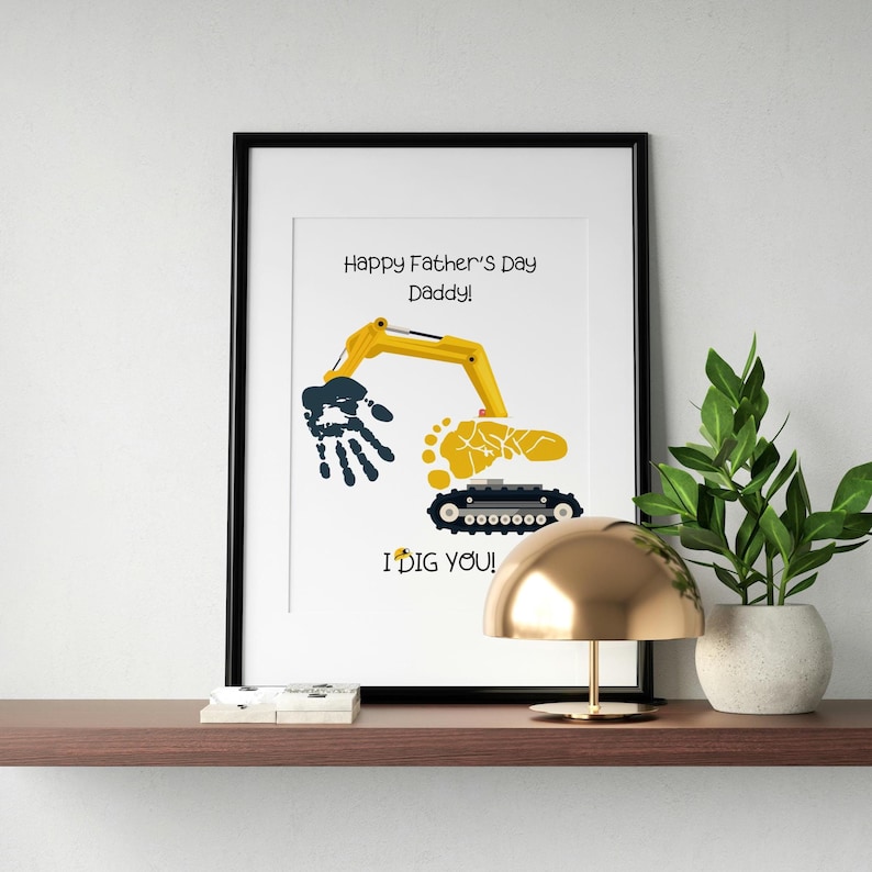 May include: Framed art print with a black border. The print features a yellow excavator arm, a handprint, and a footprint, with the text "Happy Father's Day Daddy!" and "I DIG YOU!" in black.
