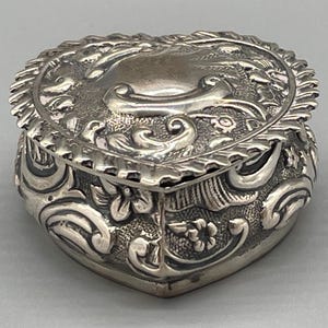 May include: A silver heart-shaped trinket box with intricate floral designs.