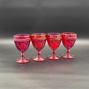 Könnte beinhalten: Vier rubinrote Vintage-Likörgläser. Jedes Glas hat ein Blumenmuster auf der Schale und einen gedrehten Stiel. Die Gläser sind aus Glas und haben eine glänzende Oberfläche. Die Gläser werden vor einem dunklen Hintergrund präsentiert.