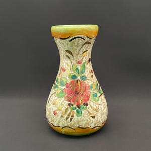 May include: A ceramic vase with a flared rim and a rounded base, featuring a cream-colored body with a speckled brown texture. The surface is decorated with a hand-painted red rose, green leaves, and yellow bands at the top and bottom edges.