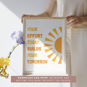 May include: A framed print with the text "YOUR EFFORT TODAY BUILDS YOUR TOMORROW" in orange. The design includes a stylized orange sun. The bottom of the frame has the text "DOWNLOAD AND PRINT ANYWHERE AND ANYTIME YOU WANT WITHOUT THE HASSLE!"