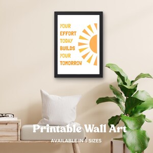 May include: A framed print with the text "YOUR EFFORT TODAY BUILDS YOUR TOMORROW" in orange. The design includes a stylized orange sun. The words "Printable Wall Art" and "AVAILABLE IN 5 SIZES" are also visible.