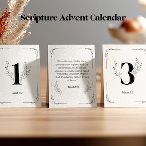 May include: A Scripture Advent Calendar with three cards displayed. Each card has a black number, floral accents, and a Bible verse reference. The first card shows the number 1 and Isaiah 9:2. The second card has a Bible verse from Isaiah 9:6. The third card shows the number 3 and Micah 5:2.
