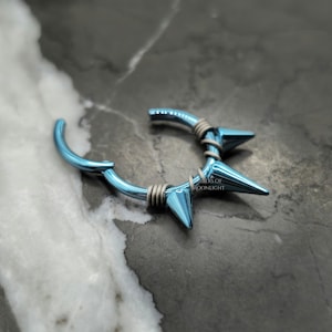 May include: A blue titanium segment ring with five sharp points, designed for ear piercings.