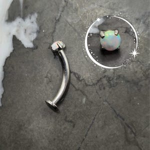 May include: A silver curved barbell with a white opal gemstone. The barbell is made of surgical steel and is suitable for body piercings.