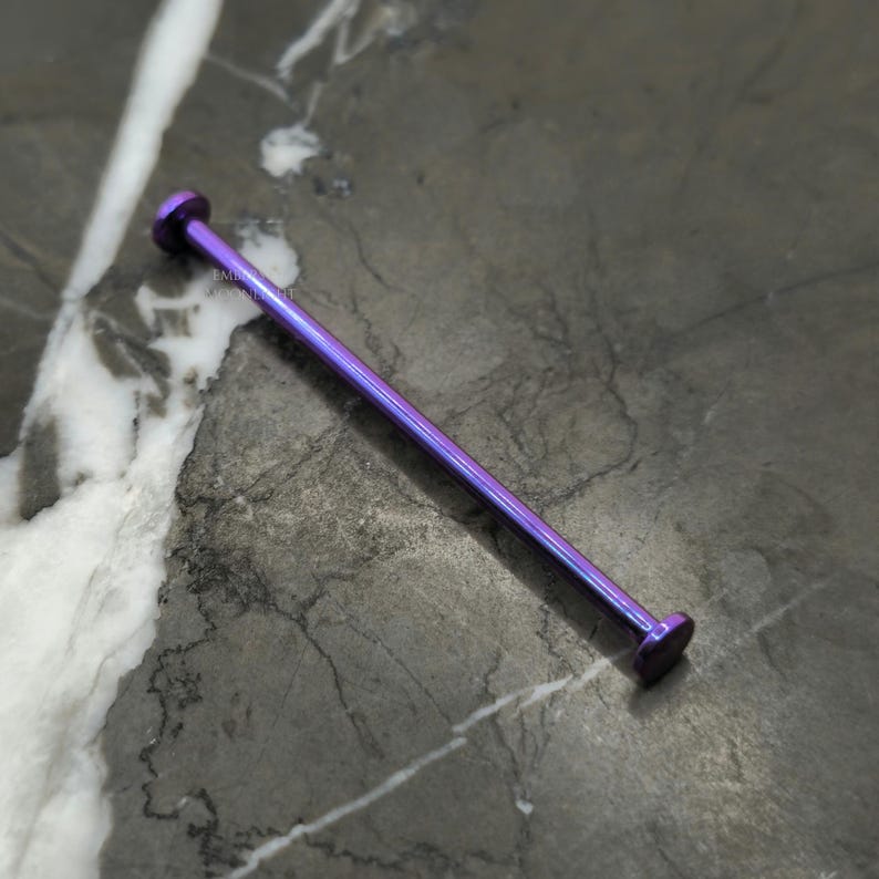 May include: A long, thin, purple-colored metal bar with rounded ends. The bar is lying on a gray and white marble surface.