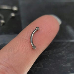 May include: A curved barbell body jewelry piece made of polished silver-toned metal. The item features a smooth, arc-shaped bar with a small, spherical bead attached to each end, creating a simple and functional design for various body piercings.