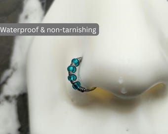 May include: A silver-toned nose ring hoop featuring four small, round, translucent teal beads secured by wire wrapping. The text 'Waterproof & non-tarnishing' is visible on the image. The jewelry is displayed on a white nose model.