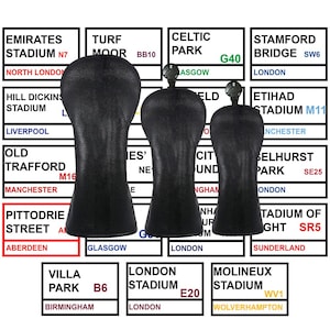 Puede incluir: Fundas negras de cuero para la cabeza del palo de golf. Las fundas tienen forma de cabeza de palo de golf y tienen un pequeño adorno metálico en la parte superior. El fondo presenta letreros con nombres y ubicaciones de estadios.