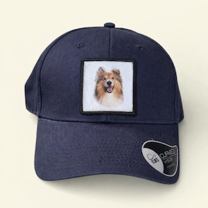 Può includere: Cappellino da baseball blu navy con una toppa quadrata con un ritratto di un cane Collie. Il cappellino ha una visiera curva e una piccola etichetta con le parole "Curved Visor".