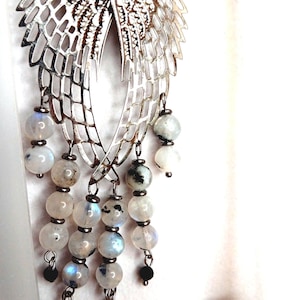 May include: Silver tone dangle earrings with a wing design and a cascade of white moonstone beads.