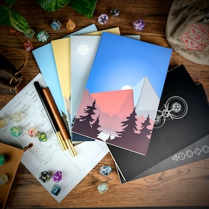 May include: A collection of notebooks with various cover designs including mountain landscapes and geometric patterns, accompanied by two pens, a character sheet, and several multi-sided dice scattered across the surface.